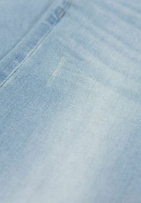 Tejido de denim azul claro con una textura suave, que presenta un ligero desgaste y un detalle de costura vertical.