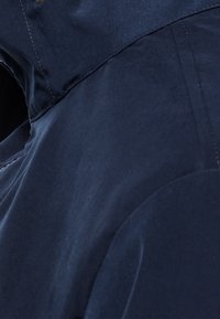 Mörkblå jacka tillverkad av ett slätt material med dragkedjestängning, minimala sömdetaljer och en mjuk textur utan synliga mönster.