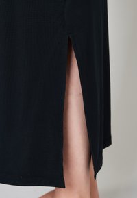 Czarna sukienka midi z bocznym rozcięciem, wykonana z miękkiej tkaniny o gładkiej fakturze, z prostym, schludnym przeszyciem na brzegu.