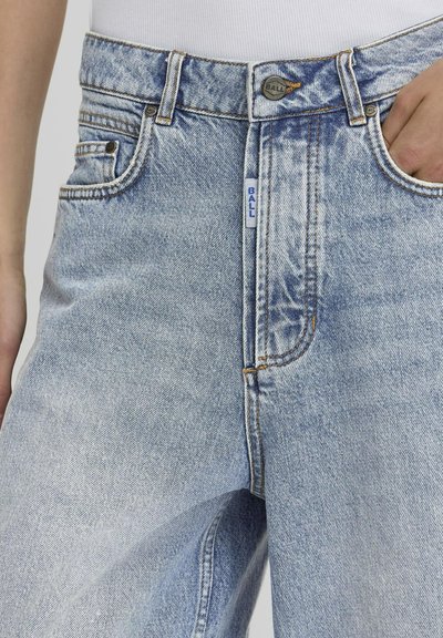 Jean en denim bleu clair avec texture déchirée, taille haute et couture de contraste. Comprend des poches à l'avant et une étiquette de logo sur la ceinture.