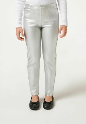 Leggings métalliques argentés avec une texture lisse et une taille élastique, associés à des chaussures plates noires avec un détail de nœud.