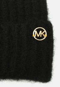 Czarna dzianinowa czapka typu beanie wykonana z miękkiego, teksturowanego materiału, z dołączonym złotym okrągłym logo z napisem "MK".