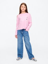 Camisa de manga longa rosa-claro com gráfico 'SISTERHOOD', combinada com jeans azuis largos e sapatos slip-on prateados, em fundo neutro.