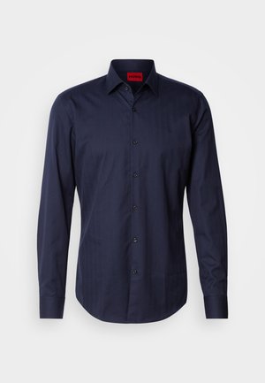 Camisa de manga longa azul-marinho com um padrão de espinha de peixe subtil, colarinho abotoado e botões pretos. Te material em mistura de algodão com uma textura suave.