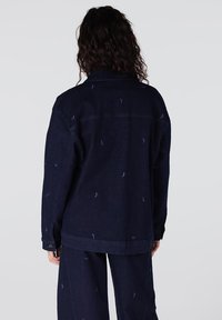 Marineblauwe spijkerjack met kleine blauwe vogelpaterns, klassieke kraag en knoopmanchetten, gecombineerd met bijpassende marineblauwe broeken.