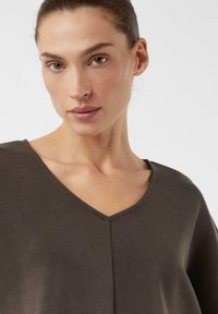 Ciemnobrązowy top z dekoltem w serek, krótkimi rękawami i miękką teksturą. Posiada minimalistyczny design oraz delikatną szwami wzdłuż przodu.