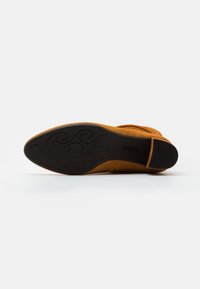 Botte cheville en suède marron avec une semelle en caoutchouc noir lisse, présentant un motif incurvé et un petit talon pour la stabilité.