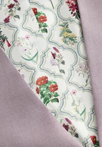 Blumenmusterstoff mit mehrfarbigen Blumen auf weißem Hintergrund, über texturiertem lilafarbenem Material drapiert.