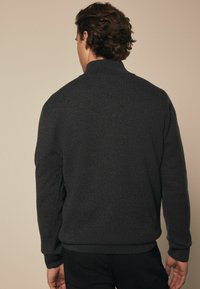 Tamno sivi pulover, teksturirana pletiva, visoki ovratnik, rebrasti manžeti i donji rub, slim fit stil, minimalistički dizajn, bez vidljive opreme.