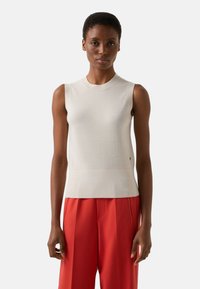 Ärmelloses cremefarbenes Oberteil mit gerippter Struktur, Rundhalsausschnitt und anliegender Silhouette; kombiniert mit locker sitzenden roten Hosen.