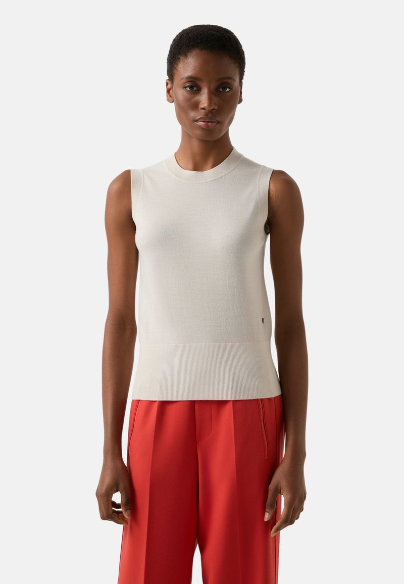 Ärmelloses cremefarbenes Oberteil mit gerippter Struktur, Rundhalsausschnitt und anliegender Silhouette; kombiniert mit locker sitzenden roten Hosen.