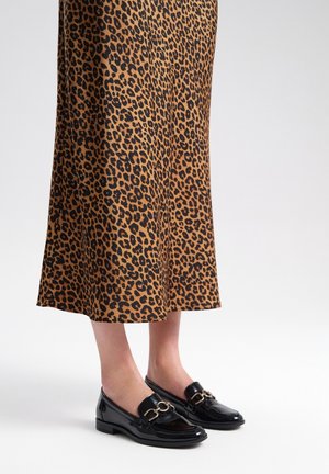 Mocasines de charol negro con un acabado brillante y detalles de hardware dorado, combinados con una falda de estampado de leopardo en tonos marrones y negros.