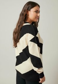 Pull noir et crème à rayures avec un motif en zigzag, composé d'un tissu doux. Doté de manches longues et d'une coupe décontractée.