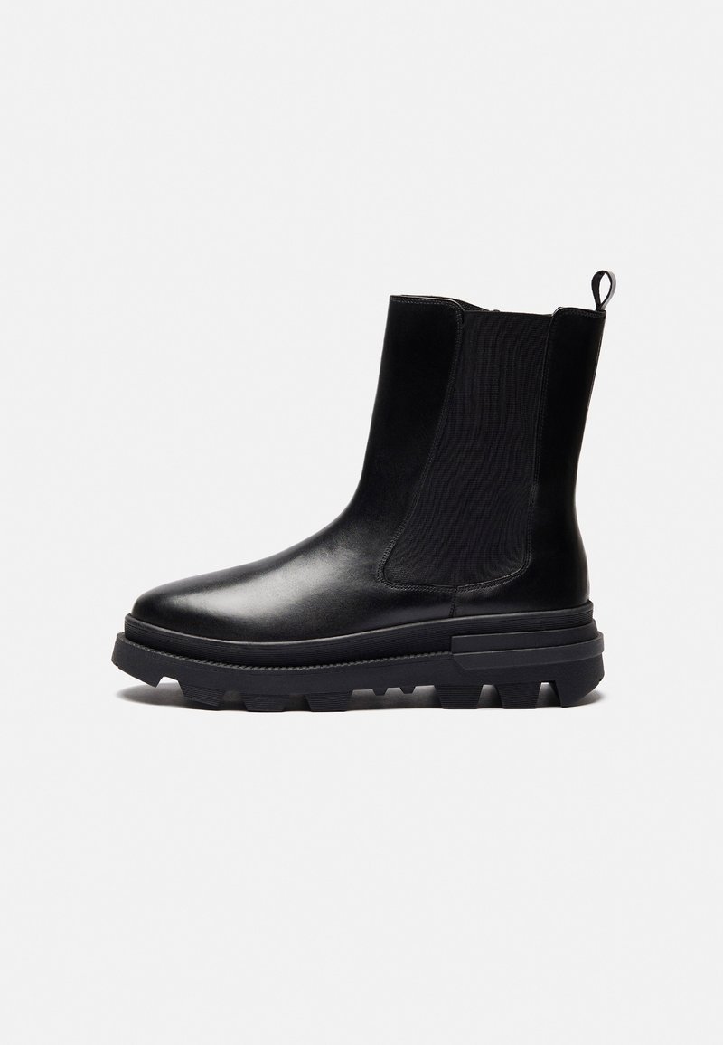 Černá kožená kotníková bota s robustní podešví, elastickými bočními panely a poutkem na zadní straně, zobrazená ze strany na bílém pozadí.