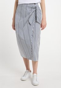 Páskovaná wrap sukně v námořnické modré a bílé barvě, s páskem na zavázání v pase, délka ke kolenům a hladká textura. Kombinována s bílými teniskami.