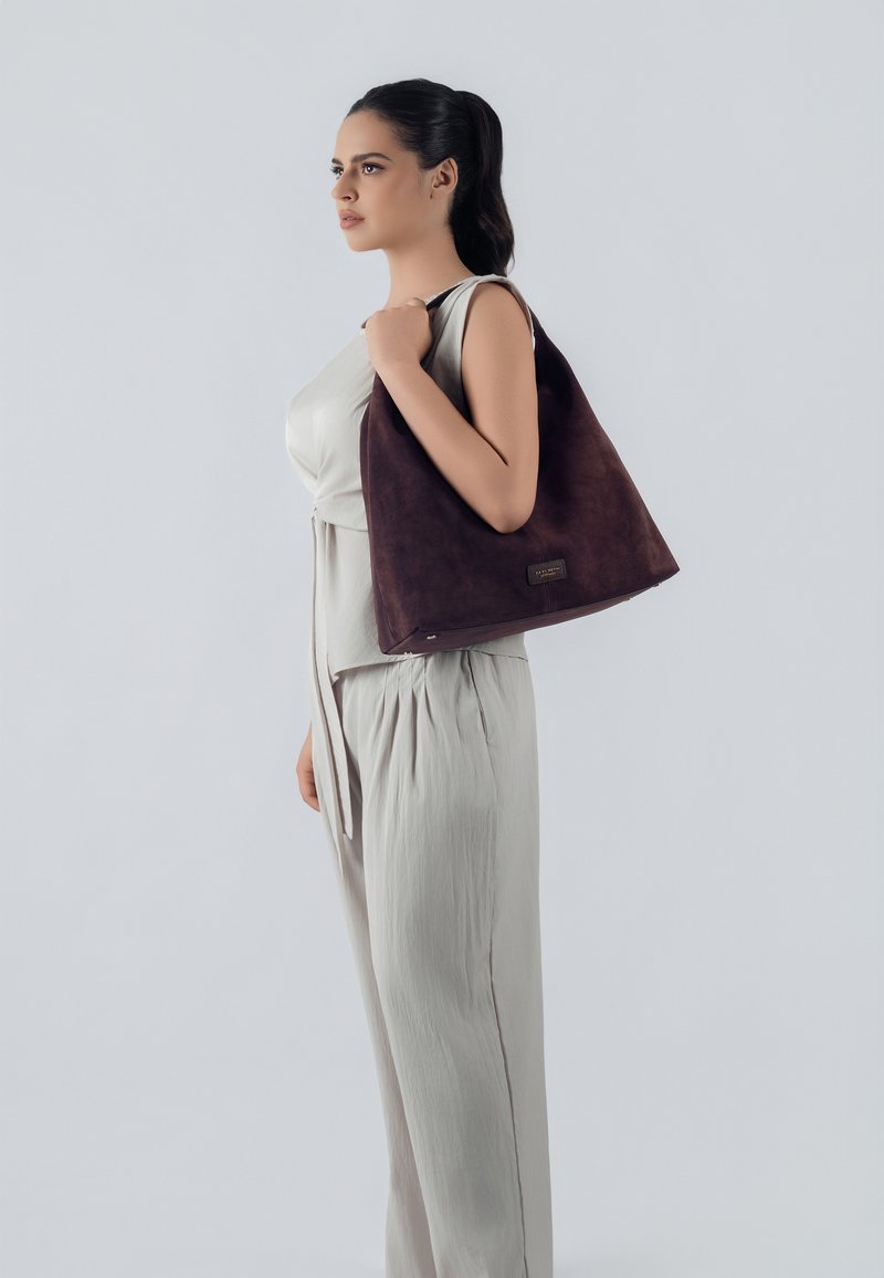 Bolso hobo de ante marrón con una textura suave, forma triangular y un acento sutil de logo. Diseño ligero y interior espacioso.