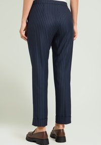 Pantaloni a righe blu navy con vestibilità su misura, dotati di tasche posteriori e risvolti, abbinati a scarpe marroni con suola spessa.