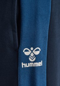 Marinblå och blå tygblandning med en slät textur; har en vit "hummel"-logotyp och grafiskt mönster på den blå delen.