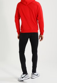 Czerwona bluza z kapturem o miękkiej teksturze, czarne jeansy slim-fit i szare sneakersy Nike z czarnymi akcentami.