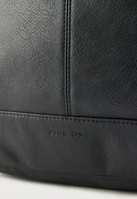 Μαύρη δερμάτινη τσάντα με υφή στην επιφάνεια, διακοσμημένη με διακριτικές ραφές και ανάγλυφο κείμενο "PIER ONE" στο κάτω μέρος.