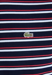 Polo en coton à rayures marines avec des rayures rouges et blanches ; comporte un petit logo de crocodile vert sur la poitrine ; en matière de coton ; texture côtelée.