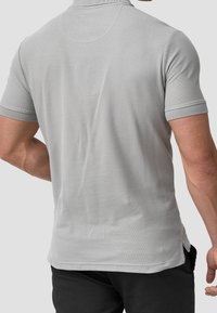 Polo gris à manches courtes en coton texturé, présentant un col classique et des fentes sur les côtés du bas pour plus de liberté de mouvement.