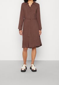 Brun, långärmad skjortklänning med krage, knappar fram och knytning i midjan, paired med beige plattformssandaler.