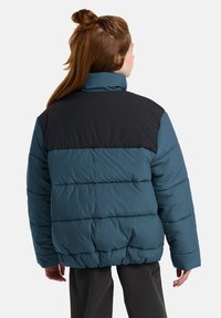 En teal dunjakke med en svart øvre del, med høy krage og horisontal søm. Myk, kviltet tekstur.