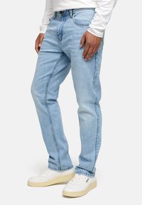 Jeans de mezclilla azul claro con un diseño de pierna recta, estilo de cinco bolsillos y un efecto de lavado sutil. Llevados con zapatillas blancas.