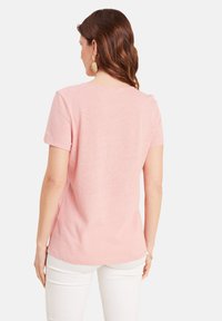 Rosa Kurzarm-T-Shirt aus weicher Baumwolle mit Rundhalsausschnitt. Kombiniert mit weißen Hosen, die ein einfaches Design und eine entspannte Passform zeigen.
