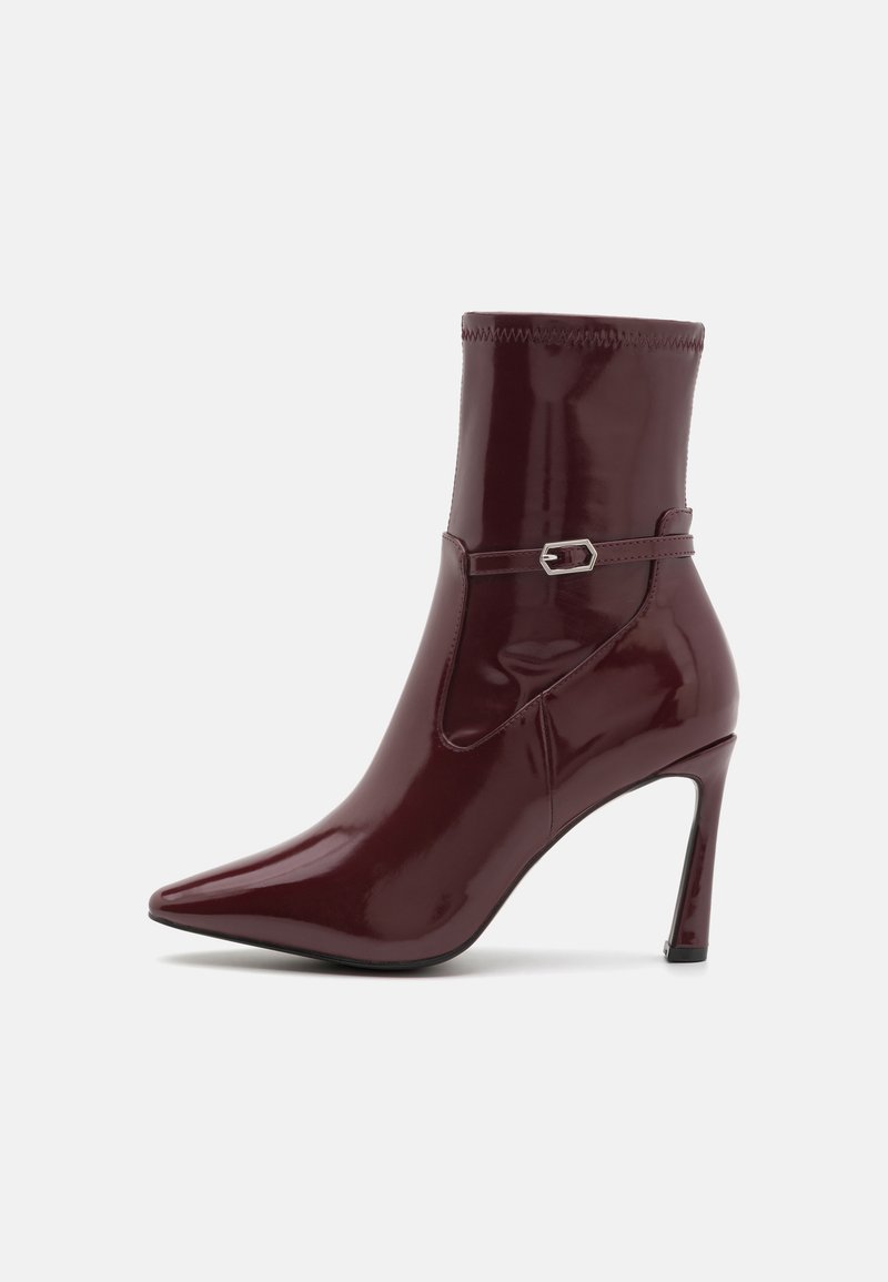 Burgundy patent leather ankle boot with a pointed toe, a slim heel, and a decorative strap with a silver buckle. Smooth texture.