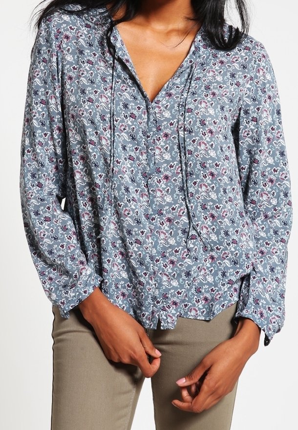 Blouse bleue à fleurs avec un col en V, des manches longues et une coupe décontractée. Présente un motif délicat avec des nuances de rose et de blanc.
