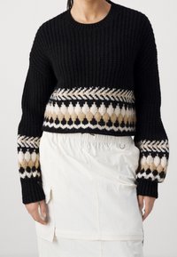 Czarny sweter dziergany o krótkim kroju, z dekoracyjnym wzorem w kolorach kremowym, beżowym i czarnym wzdłuż krawędzi i rękawów.