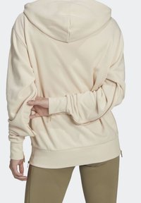 Krämfärgad hoodie med huva, långa ärmar och sidofickor med dragkedjor; har en slät, mjuk textur och en avslappnad passform.