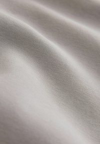 Gros plan d'un tissu gris clair lisse avec une texture côtelée fine et des plis doux créant des ombres délicates.