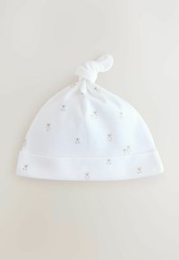 Bonnet en coton blanc pour bébé avec un sommet noué, doté d'une texture douce et de petits motifs d'ours en peluche gris clair sur l'ensemble.