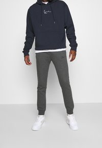 Navy hoodie with kangaroo pocket and drawstrings, gray sweatpants with logo, worn with white sneakers on a plain background.