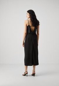 Top sans manches noir avec des pois blancs et un dos plongeant, associé à un pantalon noir taille haute. Modèle portant des talons noirs à lanières.