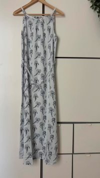 Lys grå ermeløs kjole med blomster mønster i mørk grå, med tynne stropper og knytedetalj i midjen. Glatt stofftekstur.