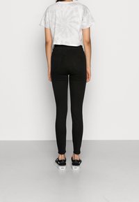 Jeans ajustados negros de cintura alta, de mezclilla; combinados con una camiseta blanca corta con diseño de tie-dye y zapatillas negras. Diseño simple, sin patrones.