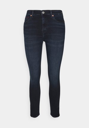 Jean slim bleu foncé avec poches avant, passants pour ceinture, fermeture par bouton, et légère décoloration sur les cuisses et les genoux.