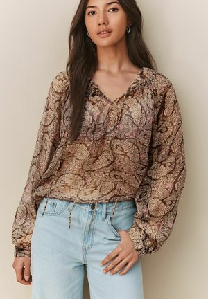 Brown and pink patterned blouse with a V-neck, smocked neckline, and long sleeves, paired with light blue jeans. Soft, flowing fabric.