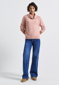 Suéter rosa claro con cuello de barco, acentos acanalados y mangas de 3/4, combinado con jeans de campana de denim y calzado marrón claro. Diseño minimalista.