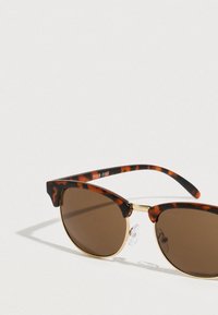 Καφέ γυαλιά ηλίου με φακούς και πλαστικό σκελετό σε σχέδιο χελώνας, με χρυσές λεπτομέρειες και μοναδικό σχεδιασμό cat-eye. Διαθέτουν ρυθμιζόμενα μαξιλαράκια μύτης.