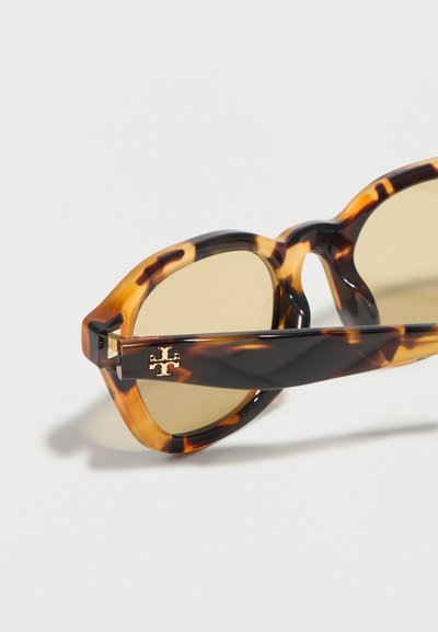 Lunettes de soleil à motif écaille de tortue avec des montures rondes et des verres marron clair, ornées d'un logo doré sur la branche.