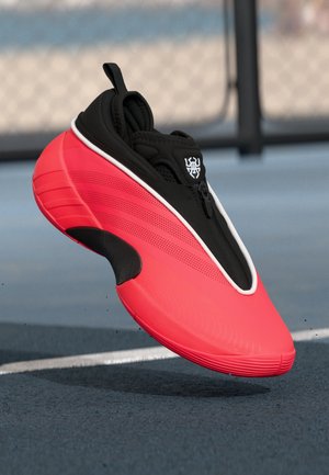 Black and red athletic shoe with a sleek design, featuring a zip closure, textured surface, and a prominent curved sole.