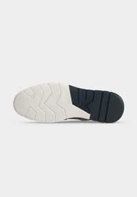 Semelle de chaussure avec l’avant blanc et le talon noir, texturée avec des motifs en zigzag et rainures droites pour l’adhérence, sur un fond clair uni.