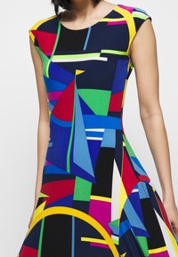 Multicolored geometric-patterned dress featuring a fitted bodice, cap sleeves, and flared hem, made from a smooth, stretchable fabric.