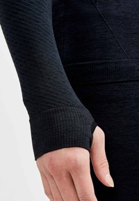 Close-up van een strak zwart longsleeve shirt met textuurstof en duimgaten in de manchetten, dat verschillende breipatronen benadrukt.