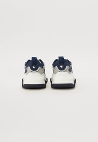 Adidași alb-albaștri cu un superior din plasă texturată, siluetă rotunjită, călcâi întărit și talpă din cauciuc pentru aderență. Include un tab cu palmă la spate.